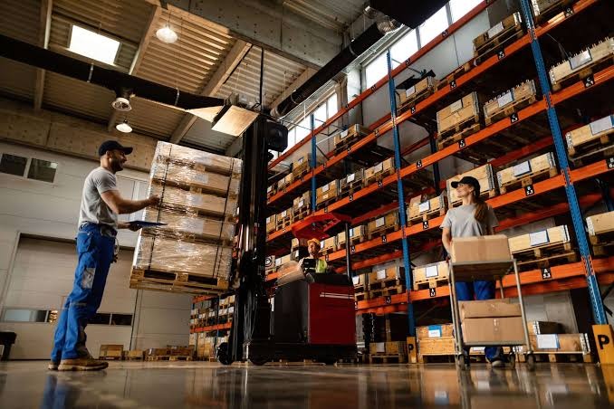 Warehouse staff with a forklift and pallets between tall orange racking