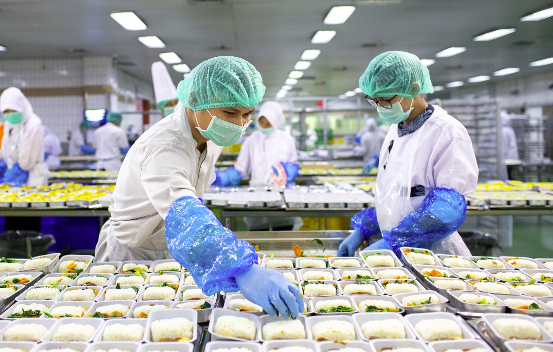 Food production workers in hairnets and gloves plating prepared meals on a packaging line
