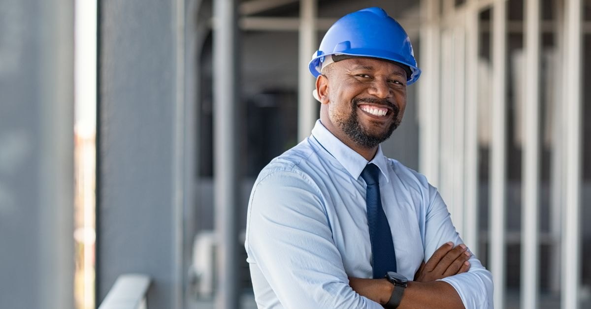 Smiling site engineer in a blue hard hat with arms crossed