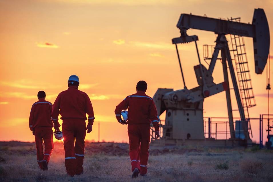 Field crew walking toward a pumpjack at sunset