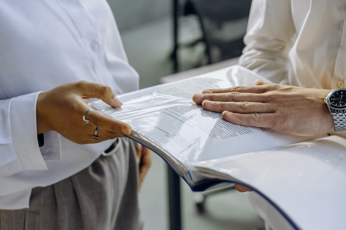 Two professionals reviewing business documents in a binder
